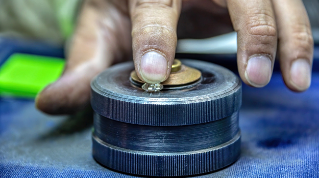 A polished diamond under a worker’s finger. (Shutterstock)